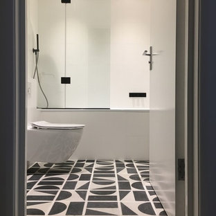 Immagine di una piccola stanza da bagno minimalista con ante lisce, vasca da incasso, vasca/doccia, WC sospeso, pistrelle in bianco e nero, piastrelle in ceramica, pareti bianche, pavimento con piastrelle in ceramica, lavabo sospeso e top in superficie solida