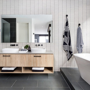 Foto de cuarto de baño contemporáneo con bañera exenta, suelo gris, armarios con paneles lisos, puertas de armario de madera clara, baldosas y/o azulejos blancos, lavabo sobreencimera y encimeras grises