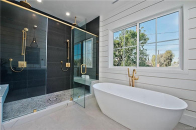 Cette image montre une grande salle de bain principale minimaliste avec une baignoire indépendante, une douche double, un carrelage noir, un mur blanc, un sol blanc, une cabine de douche à porte battante, un banc de douche et du lambris de bois.