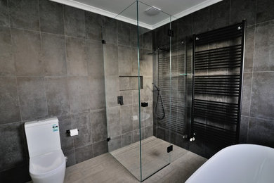 Modelo de cuarto de baño principal minimalista de tamaño medio con ducha esquinera, sanitario de una pieza, baldosas y/o azulejos grises, baldosas y/o azulejos de porcelana, paredes grises y suelo de baldosas de porcelana