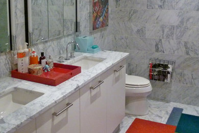ニューヨークにある中くらいなエクレクティックスタイルのおしゃれな浴室 (フラットパネル扉のキャビネット、白いキャビネット、グレーの壁、磁器タイルの床、アンダーカウンター洗面器、大理石の洗面台、グレーの床) の写真