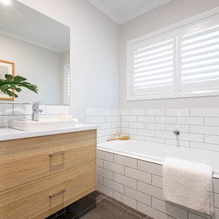 Contemporary 3/4 bathroom in Other with flat-panel cabinets, medium wood cabinets, a drop-in tub, subway tile, a vessel sink, grey floor and white benchtops.