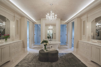 Пример оригинального дизайна: огромная главная ванная комната в классическом стиле с плоскими фасадами, белыми фасадами, отдельно стоящей ванной, двойным душем, раздельным унитазом, бежевой плиткой, каменной плиткой, бежевыми стенами, мраморным полом, врезной раковиной и мраморной столешницей