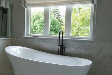 На фото: огромная главная ванная комната в классическом стиле с фасадами в стиле шейкер, белыми фасадами, отдельно стоящей ванной, двойным душем, унитазом-моноблоком, белой плиткой, керамогранитной плиткой, серыми стенами, полом из керамогранита, врезной раковиной, мраморной столешницей, серым полом, душем с распашными дверями и белой столешницей с