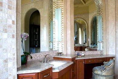 Immagine di un'ampia stanza da bagno padronale mediterranea con lavabo sottopiano, ante con bugna sagomata, ante in legno bruno, top in marmo, piastrelle beige, piastrelle in ceramica, pareti beige e pavimento in travertino