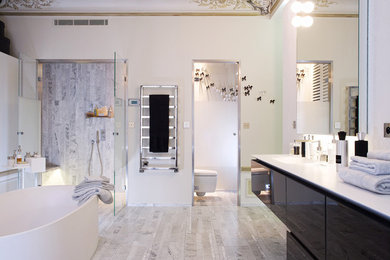 Modelo de cuarto de baño principal contemporáneo con lavabo integrado, puertas de armario negras, bañera exenta, ducha abierta, sanitario de pared, baldosas y/o azulejos grises, paredes blancas y suelo de mármol