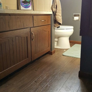 Lantlig inredning av ett litet badrum med dusch, med luckor med infälld panel, bruna skåp, ett platsbyggt badkar, en toalettstol med separat cisternkåpa, gul kakel, keramikplattor, grå väggar, vinylgolv, ett nedsänkt handfat och laminatbänkskiva
