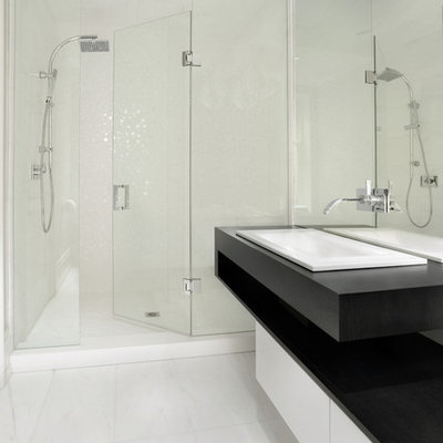 Example of a mid-sized trendy 3/4 white tile marble floor and white floor alcove shower design in Toronto with a drop-in sink, flat-panel cabinets, white cabinets, solid surface countertops and black countertops