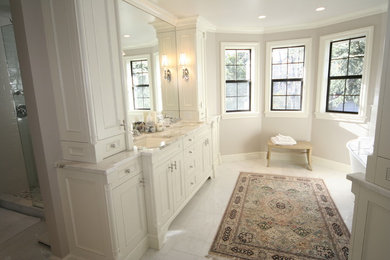 Modelo de cuarto de baño principal clásico grande con lavabo bajoencimera, puertas de armario blancas, bañera esquinera, paredes blancas, suelo de mármol, armarios con rebordes decorativos y encimera de mármol