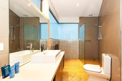 Foto på ett funkis badrum, med en öppen dusch, en toalettstol med separat cisternkåpa, bruna väggar, ett fristående handfat, med dusch som är öppen, släta luckor och brun kakel