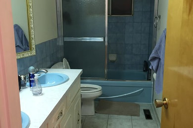 Example of a mid-sized trendy master gray tile and porcelain tile travertine floor bathroom design in Edmonton with flat-panel cabinets, gray cabinets, a one-piece toilet, white walls, a drop-in sink and quartz countertops
