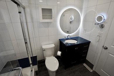 This is an example of a small contemporary ensuite bathroom in Columbus with shaker cabinets, black cabinets, an alcove bath, a shower/bath combination, a one-piece toilet, white tiles, ceramic tiles, white walls, ceramic flooring, a submerged sink, quartz worktops, grey floors, a sliding door, blue worktops, a shower bench, a single sink and a freestanding vanity unit.