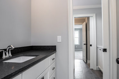 Foto de cuarto de baño de tamaño medio con puertas de armario blancas, paredes grises, suelo vinílico, aseo y ducha, lavabo bajoencimera, encimera de granito, suelo gris y encimeras negras
