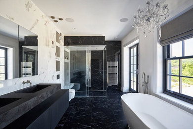 Photo of a contemporary bathroom in Essex with a freestanding bath, a built-in shower, a wall mounted toilet, black and white tiles, porcelain tiles, porcelain flooring, a wall-mounted sink, solid surface worktops, black floors, a sliding door and multi-coloured worktops.