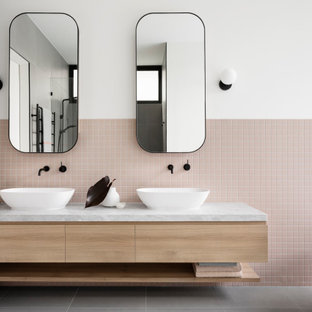 Inspiration for a contemporary bathroom in Melbourne with flat-panel cabinets, light wood cabinets, a freestanding tub, pink tile, mosaic tile, white walls, a vessel sink, grey floor, white benchtops, a double vanity and a floating vanity.