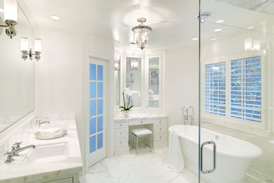 Modelo de cuarto de baño tradicional con lavabo bajoencimera, armarios con paneles empotrados, puertas de armario blancas, encimera de mármol, bañera exenta, ducha empotrada y baldosas y/o azulejos blancos