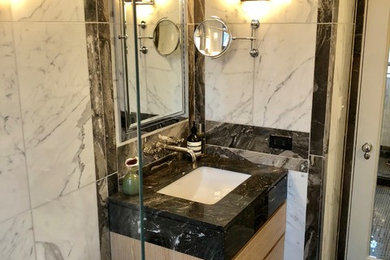 Example of a mid-sized trendy white tile and marble tile mosaic tile floor and black floor bathroom design in New York with flat-panel cabinets, light wood cabinets, a two-piece toilet, white walls, an undermount sink, marble countertops and black countertops