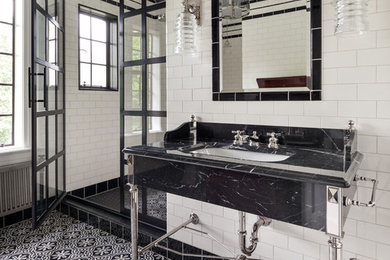 Foto di una stanza da bagno padronale industriale con piastrelle bianche, piastrelle in ceramica, pareti bianche, pavimento in cementine, lavabo a consolle, top in marmo, pavimento nero e porta doccia a battente