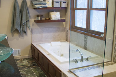 This is an example of a large modern ensuite bathroom in Minneapolis with flat-panel cabinets, brown cabinets, a hot tub, a walk-in shower, a two-piece toilet, multi-coloured tiles, glass tiles, beige walls, marble flooring, a vessel sink and granite worktops.