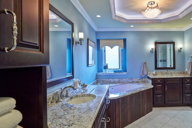 Example of a large transitional master ceramic tile and beige floor bathroom design in Chicago with raised-panel cabinets, dark wood cabinets, an undermount tub, blue walls, an undermount sink and granite countertops