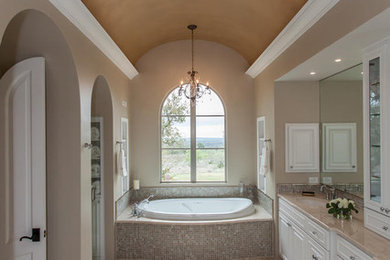 Elegant beige tile and mosaic tile drop-in bathtub photo in Austin with white cabinets