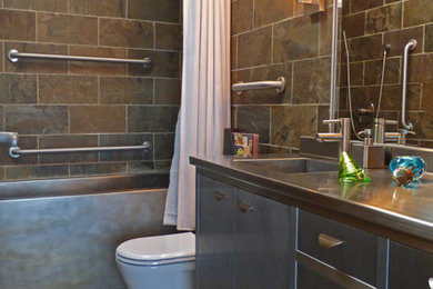 Esempio di una piccola stanza da bagno padronale minimalista con lavabo integrato, ante lisce, ante grigie, top in acciaio inossidabile, vasca ad alcova, vasca/doccia, WC monopezzo, piastrelle grigie, piastrelle in pietra, pareti verdi e pavimento in ardesia