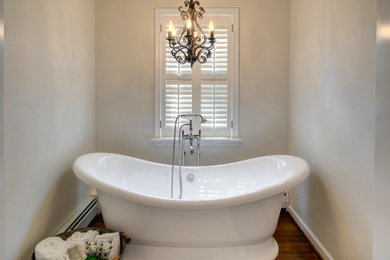 Trendy medium tone wood floor freestanding bathtub photo in Philadelphia with beige walls