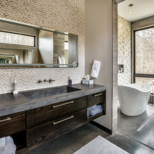 Example of a trendy master beige tile and pebble tile concrete floor and gray floor freestanding bathtub design in Other with flat-panel cabinets, dark wood cabinets, an integrated sink, concrete countertops and beige walls