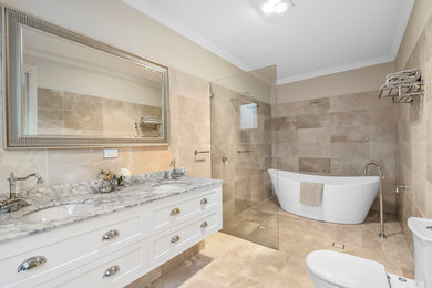 This is an example of a large contemporary ensuite bathroom in Orange County with flat-panel cabinets, white cabinets, a freestanding bath, a walk-in shower, beige tiles, stone tiles, a built-in sink, marble worktops, an open shower, white worktops, a one-piece toilet, beige walls, slate flooring and beige floors.