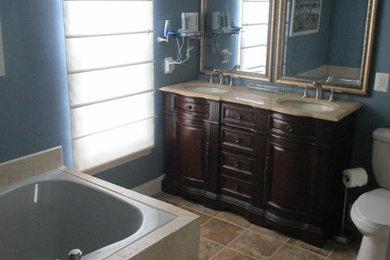 Mid-sized trendy stone tile porcelain tile drop-in bathtub photo in DC Metro with a console sink, furniture-like cabinets, medium tone wood cabinets, granite countertops, a two-piece toilet and blue walls