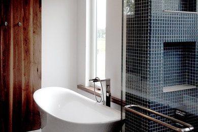 Modern inredning av ett badrum, med ett fristående badkar, svart kakel, glaskakel, vita väggar, mellanmörkt trägolv, brunt golv och dusch med skjutdörr