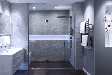 This is an example of a large contemporary ensuite bathroom with flat-panel cabinets, white cabinets, an alcove bath, a built-in shower, a one-piece toilet, grey tiles, porcelain tiles, grey walls, porcelain flooring, an integrated sink, brown floors, a hinged door and white worktops.