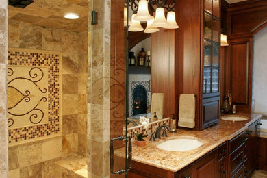 Modelo de cuarto de baño tradicional con lavabo bajoencimera, armarios con paneles con relieve, puertas de armario con efecto envejecido, encimera de granito, bañera encastrada y ducha a ras de suelo