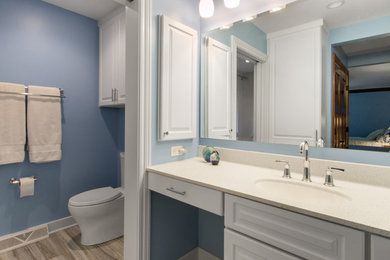This is an example of a medium sized nautical shower room bathroom in Milwaukee with raised-panel cabinets, white cabinets, engineered stone worktops, an alcove bath, an alcove shower, a one-piece toilet, blue walls, porcelain flooring, a submerged sink, brown floors, beige tiles, a shower curtain and beige worktops.