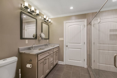Example of a mid-sized transitional master gray tile and porcelain tile porcelain tile and gray floor bathroom design in New Orleans with shaker cabinets, gray cabinets, a two-piece toilet, gray walls, an undermount sink, quartzite countertops and a hinged shower door