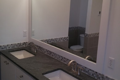 Photo of a large modern ensuite bathroom in Minneapolis with flat-panel cabinets, white cabinets, a built-in bath, a corner shower, a two-piece toilet, grey tiles, porcelain tiles, white walls, porcelain flooring, a submerged sink and granite worktops.