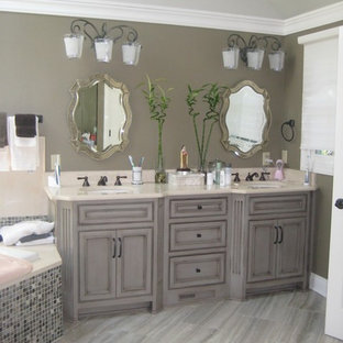 Mittelgroßes Shabby-Style Badezimmer En Suite mit Kassettenfronten, grauen Schränken, Einbaubadewanne, Eckdusche, beigefarbenen Fliesen, Steinplatten, Mineralwerkstoff-Waschtisch, Falttür-Duschabtrennung, Wandtoilette mit Spülkasten, brauner Wandfarbe, Porzellan-Bodenfliesen, Unterbauwaschbecken und braunem Boden in Cleveland