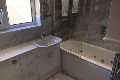 Design ideas for a small contemporary family bathroom in Cambridgeshire with flat-panel cabinets, white cabinets, grey tiles, porcelain tiles, porcelain flooring, solid surface worktops and grey floors.