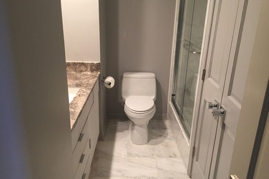 Cette photo montre une petite salle de bain chic avec un placard à porte plane, des portes de placard blanches, WC à poser, un carrelage blanc, un carrelage de pierre, un mur gris, un sol en marbre, un lavabo encastré et un plan de toilette en marbre.