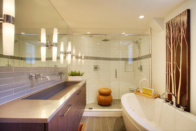 This is an example of a modern ensuite bathroom in Seattle with flat-panel cabinets, medium wood cabinets, engineered stone worktops, white tiles, glass tiles, a freestanding bath, a walk-in shower, a two-piece toilet, an integrated sink, white walls and porcelain flooring.