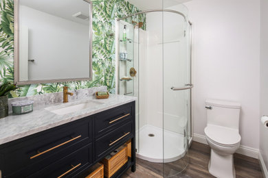 Example of a mid-sized mid-century modern 3/4 vinyl floor, brown floor, single-sink and wallpaper corner shower design in San Diego with shaker cabinets, black cabinets, a one-piece toilet, white walls, a drop-in sink, quartzite countertops, a hinged shower door, gray countertops and a freestanding vanity
