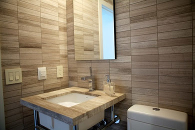 Ispirazione per una stanza da bagno padronale minimalista di medie dimensioni con lavabo sottopiano, vasca idromassaggio, vasca/doccia, WC a due pezzi, piastrelle marroni, pareti beige e top in legno