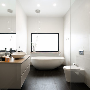 This is an example of a contemporary master bathroom in Adelaide with flat-panel cabinets, beige cabinets, a freestanding tub, an open shower, a one-piece toilet, white tile, a vessel sink, wood benchtops, black floor, an open shower and beige benchtops.