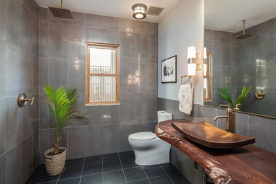 Bathroom - mid-sized rustic 3/4 gray tile and ceramic tile porcelain tile and black floor bathroom idea in Phoenix with a two-piece toilet, gray walls, a vessel sink and wood countertops