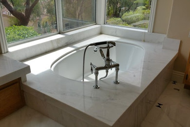 Aménagement d'une salle de bain principale classique en bois brun avec un placard avec porte à panneau surélevé, une baignoire d'angle, un mur beige, un sol en marbre, un lavabo encastré et un plan de toilette en marbre.