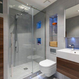 Cette photo montre une petit salle de bain tendance avec un placard à porte plane, des portes de placard marrons, une douche d'angle, un WC suspendu, un carrelage gris, un mur gris, un sol gris, une cabine de douche à porte coulissante et un lavabo intégré.
