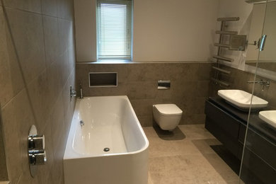 This is an example of a large contemporary ensuite bathroom in Hampshire with dark wood cabinets, a built-in bath, a walk-in shower, a wall mounted toilet, grey tiles, porcelain tiles, white walls, porcelain flooring, a console sink and quartz worktops.