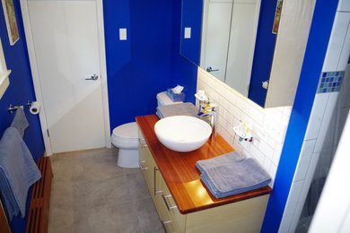 Modelo de cuarto de baño minimalista con sanitario de dos piezas, baldosas y/o azulejos blancos, baldosas y/o azulejos de cemento, paredes azules, lavabo sobreencimera y encimera de madera
