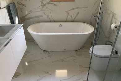 Mid-sized minimalist master white tile and marble tile marble floor and white floor bathroom photo in New York with flat-panel cabinets, white cabinets, a one-piece toilet, white walls, an undermount sink and marble countertops