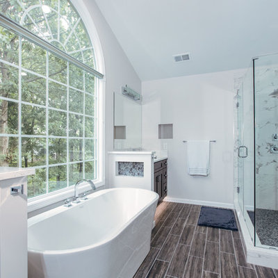 Example of a large minimalist master white tile and porcelain tile porcelain tile and brown floor bathroom design in DC Metro with shaker cabinets, dark wood cabinets, a two-piece toilet, gray walls, an undermount sink, quartz countertops, a hinged shower door and white countertops